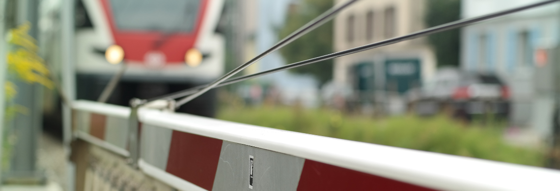 Man sieht einen Zug und eine Bahnschranke.